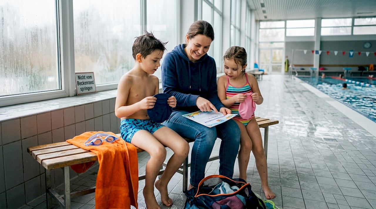 Am Beckenrand begutachtet die Familie gemeinsam die Schwimmabzeichen ihrer Kinder.