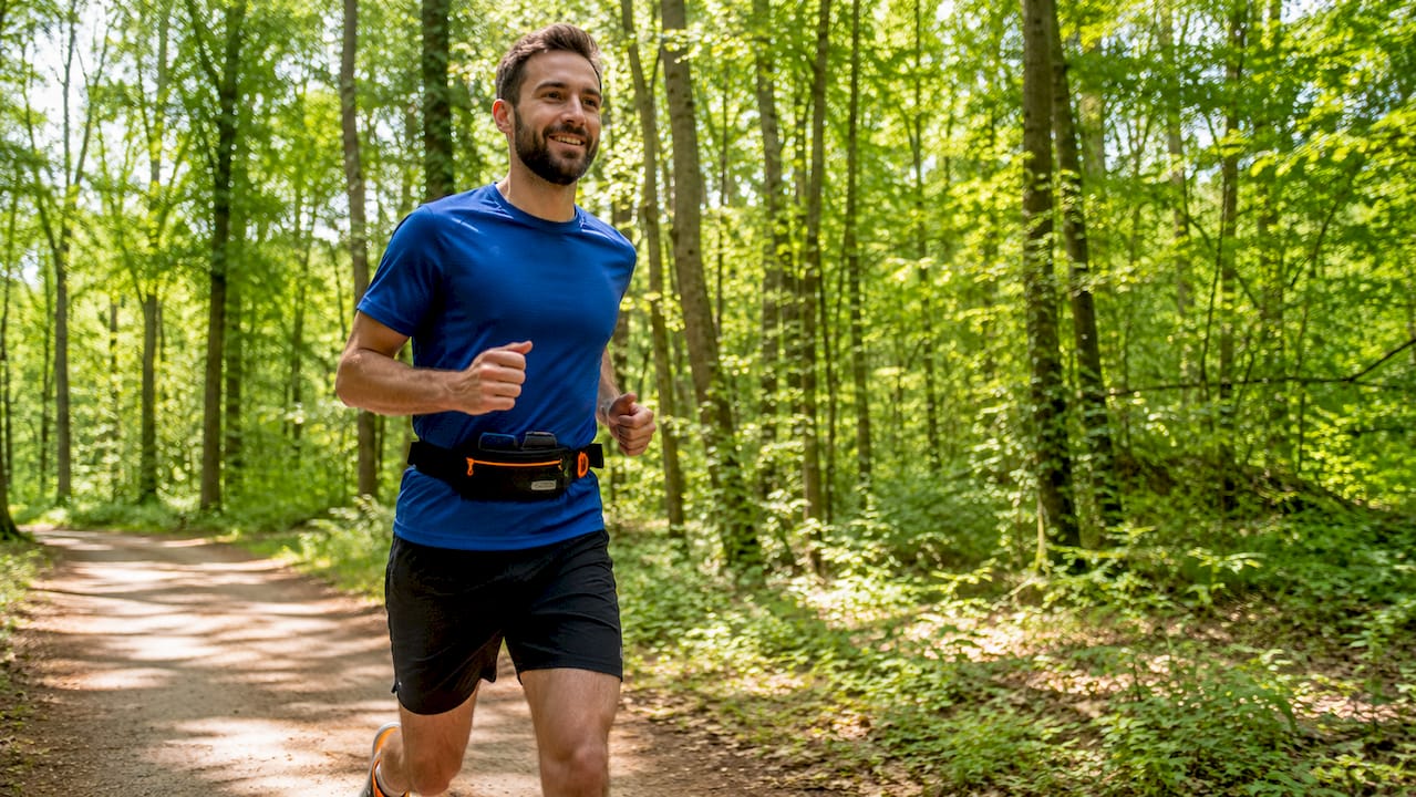 Ein Läufer mit Hüftgurt joggt entspannt durch den Park.