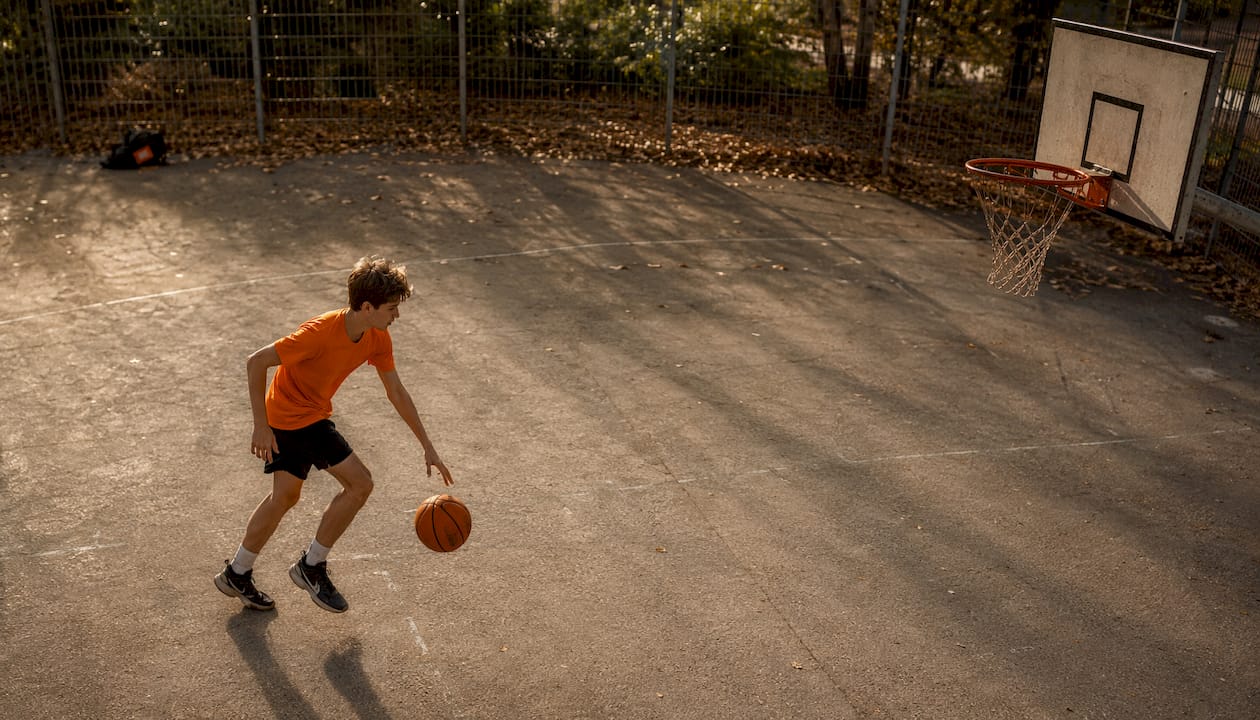 Ein Teenager zockt Basketball auf dem Schulhof.