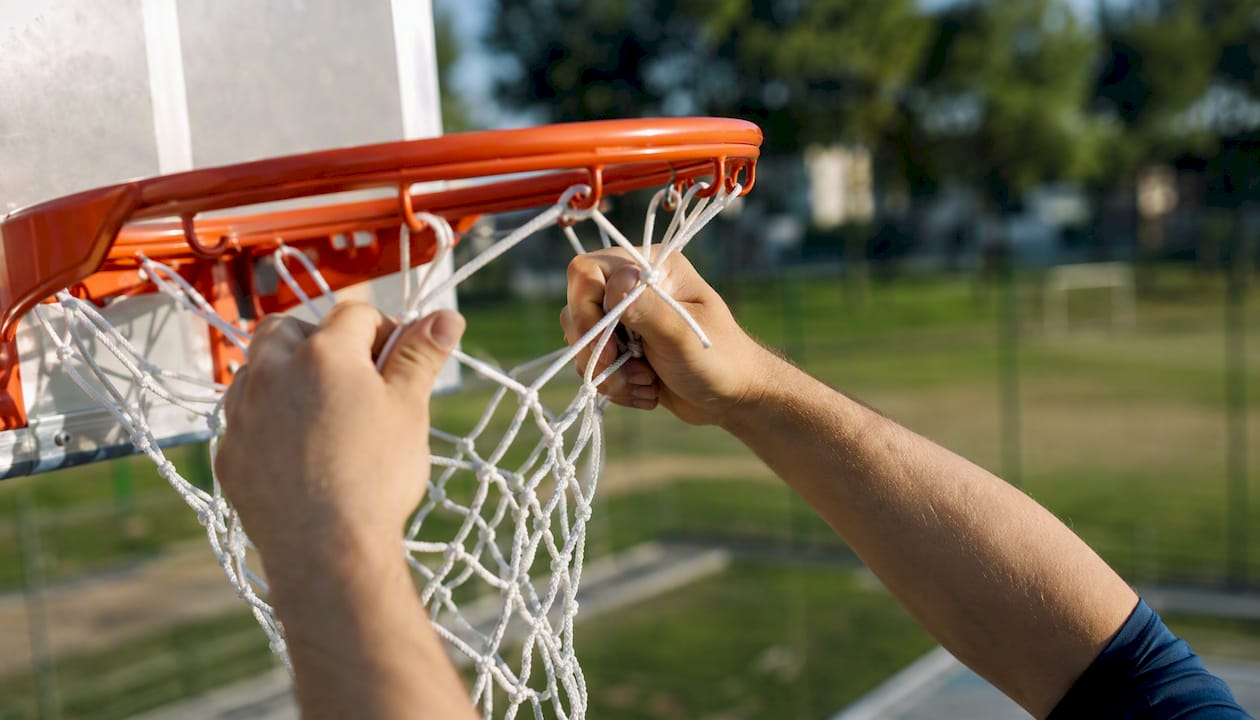 Jemand befestigt das Netz am Basketballkorb.