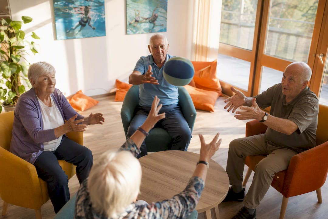 Ältere Menschen spielen gemeinsam ein Ballspiel im Aufenthaltsraum.