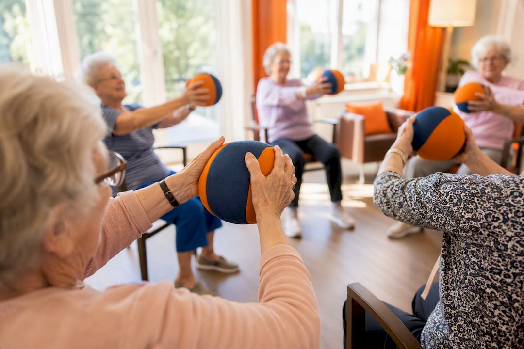 Senioren sitzen im Kreis und geben sich einen weichen Ball weiter