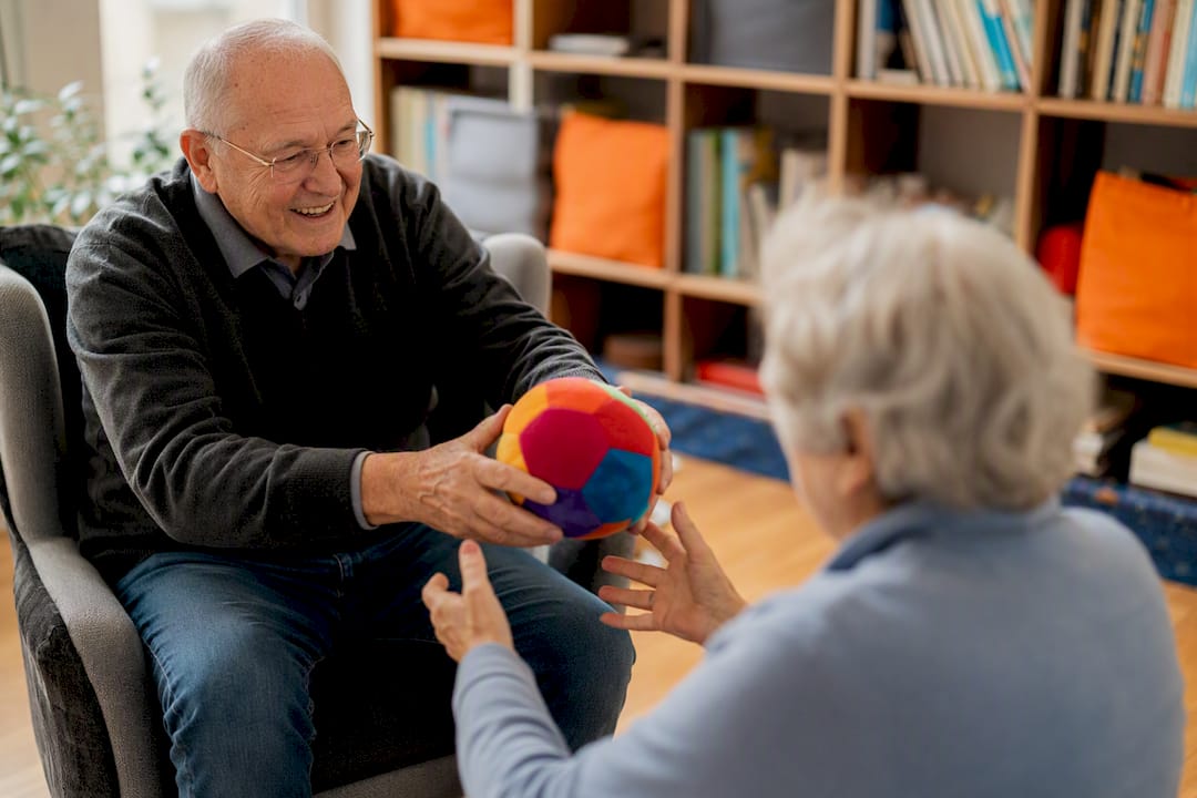 Betreuer reicht buntes Ball an sitzende Senioren weiter